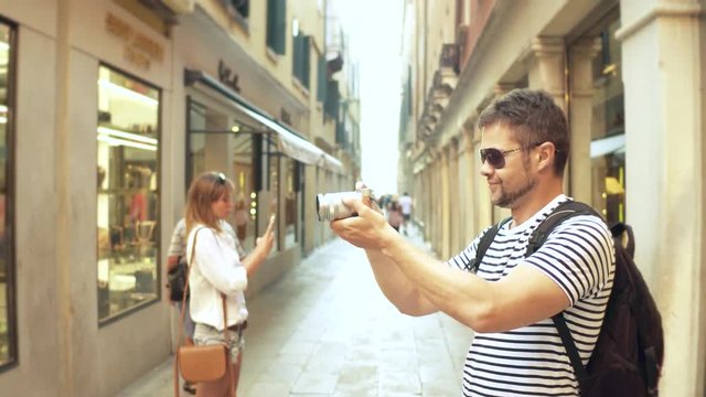 Young handsome bearded man making photos of a narrow street with his camera