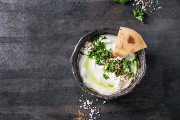  labneh middle eastern lebanese cream cheese dip with olive oil, salt, herbs served traditional pita bread in terracotta bowl over dark texture metal background. Top view with space © Natasha Breen