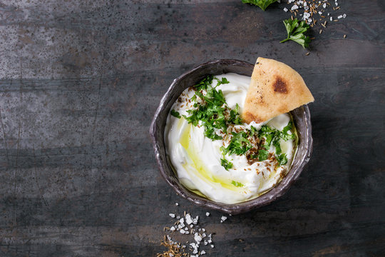 Fototapeta labneh middle eastern lebanese cream cheese dip with olive oil, salt, herbs served traditional pita bread in terracotta bowl over dark texture metal background. Top view with space
