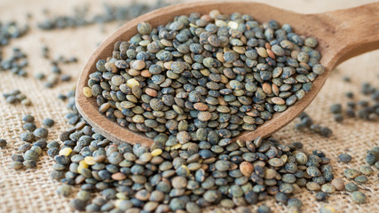 French lentils from wooden spoon spill on sackcloth