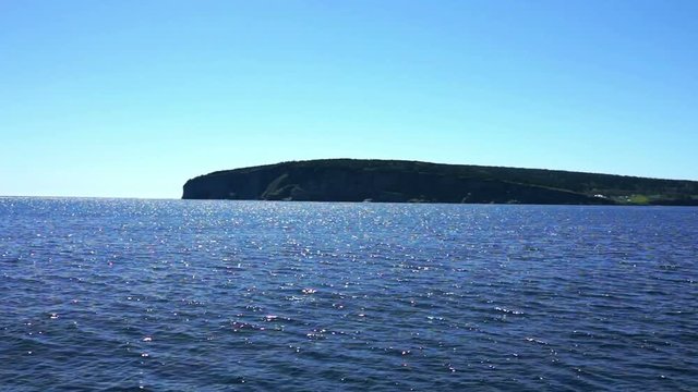 View from moving boat on Bonaventure Island coast cliffs in Gaspe, Quebec, Canada, Gaspesie region with morning sunlight shadow, waves at Gulf of Saint Lawrence