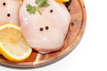 raw chicken breast, lemon, pepper on wooden plate on white background
