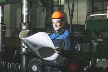 Working in production against a background of machines from the engineering drawings in his hands...