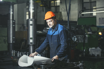 Working in production against a background of machines from the engineering drawings in his hands while working