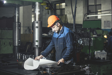 Working in production against a background of machines from the engineering drawings in his hands while working