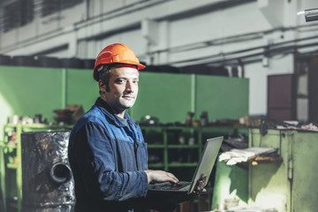 Working in the plant with a laptop in hand on the background of the equipment