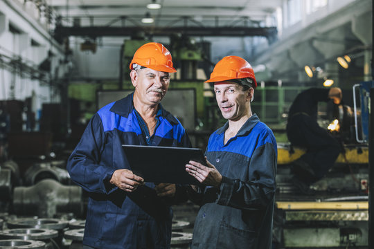 Two workers at an industrial plant with a tablet in hand, working together manufacturing activities