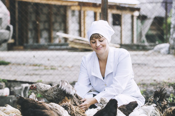 Woman in Bathrobe smiling young veterinarian checks the hens on a small private farm