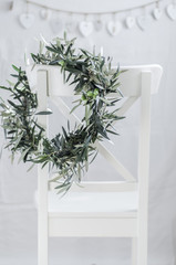 Corona de ramas de olivo sobre silla blanca con decoración en el fondo