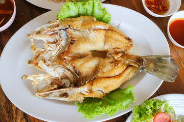 deep fried snapper fish with fish sauce and green lettuce on white dish