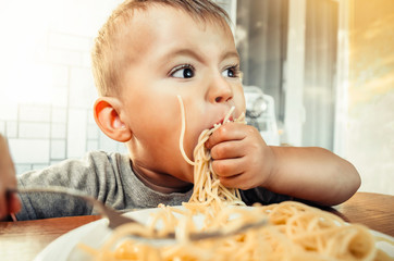 Baby in the kitchen eagerly eating pasta