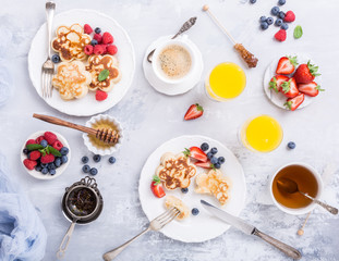 Flat lay with breakfast with scotch pancakes in flower form, berries and honey on light wooden table. Healthy food concept with copy space.