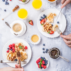 Fototapeta na wymiar Flat lay with scotch pancakes in flower form, berries and honey with human hands. Healthy breakfast concept. Women eating together, top view.