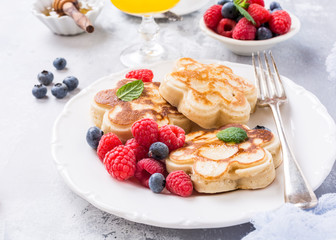Scotch pancakes in flower form with berries and honey on white wooden background. Healthy breakfast concept.