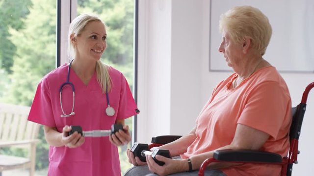 Nurse in residential care home showing elderly lady in wheelchair some exercises with weights.