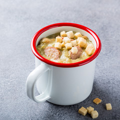 Delicious homemade pea soup with sausage and croutons in enamel mug. Healthy food concept with copy space.