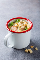 White enamel mug with delicious homemade pea soup with sausage and croutons. Healthy food concept.