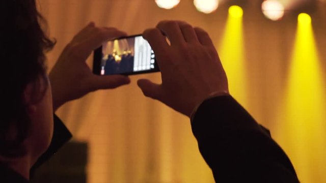 Hands of a person filming a singer performing on stage. A hands of a man live streaming a pop star singing and audience dancing in the club