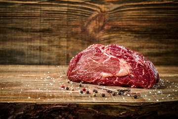 Dry aged Ribeye Steak with seasoning on wooden background.