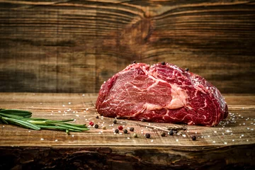 Poster Dry aged Ribeye Steak with seasoning on wooden background. © nazarovsergey