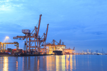 crane loading merchandise to boat in port during morning time background with refinery plant