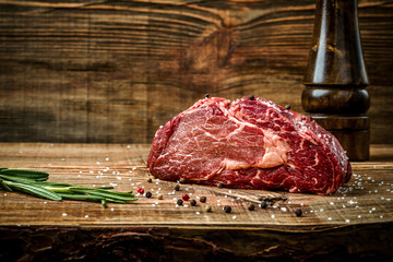 Dry aged Ribeye Steak with seasoning on wooden background.