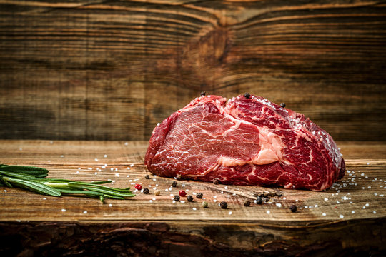 Dry aged Ribeye Steak with seasoning on wooden background.
