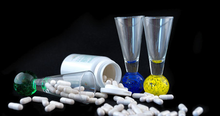 Medical pills and liquor glasses with tablet bottle, isolated on black. Alcohol and medical concept