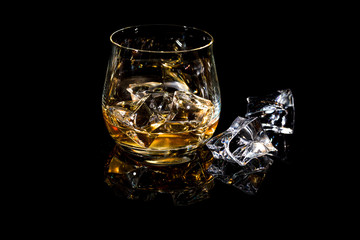 ein Glas mit Whiskey auf Eis vor schwarzem Hintergrund