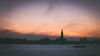 Fototapeta na wymiar Italian silhouette of Venice at sunset with boats, Italian city panorama vintage shot from sea and sky, Sunset in Venice background, Dark scene of Venice skyline, Symbol of evening Venice
