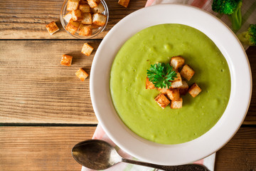 Broccoli cream soup with croutons in plate on rustic wooden table