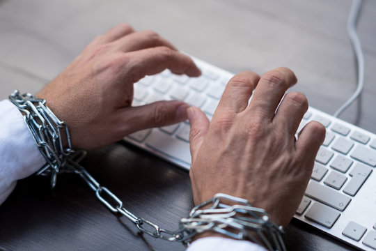 Businessman hands tied with chains on laptop keyboard