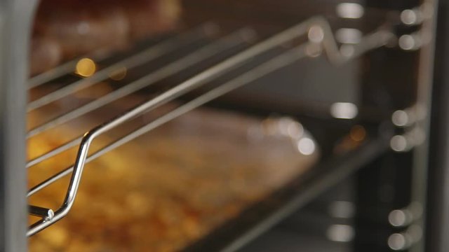 Cooking beef sausages in the oven with broiler closeup. Chef takes out grilled juicy sausages on grilling rack from the oven. Food preparation in electric cooker.