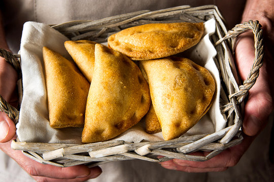 Man chef holding in hands a wicker basket with freshly baked vegetarian empanadas turnover pies with vegetables cheese in tomato sauce. Authentic kinfolk atmosphere. Cozy home.