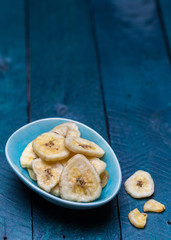 Getrocknete Banane in einer Schale auf petrolfarbenem Holzuntergrund