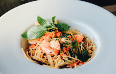 spaghetti pasta with shrimps and sweet basil on white plate over wooden table