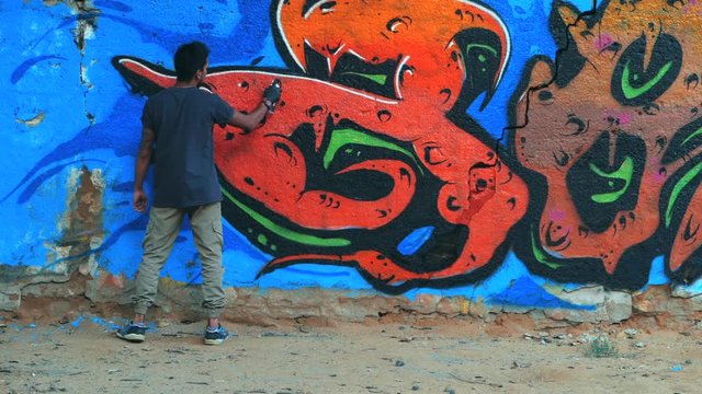 Creative art - teenage boy painting colorful abstract ornament graffiti on street wall with aerosol spray. Slow motion. Handheld 1920x1080 cinematic toned HD footage. Back view, overall plan