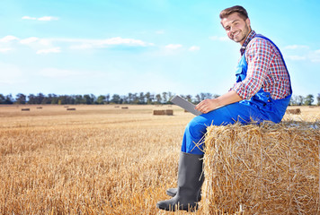 Naklejka na ściany i meble Young male farmer holding laptop in wheat field