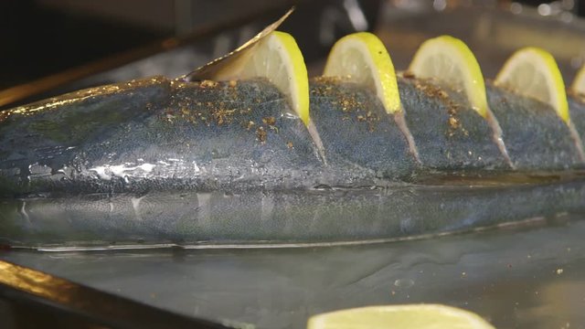 Cooking whole roasted fish seriola with lemon baked in the oven. Chef puts a baking sheet with raw amberjack into the hot oven. Food preparation with electric cooker.