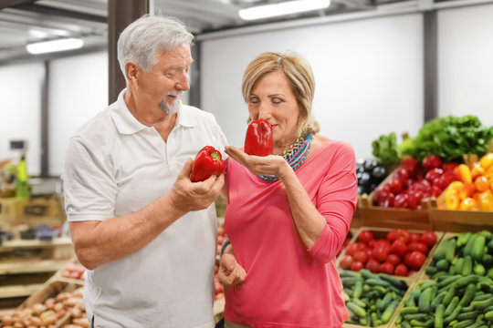 Happy senior couple choosing vegetables at market