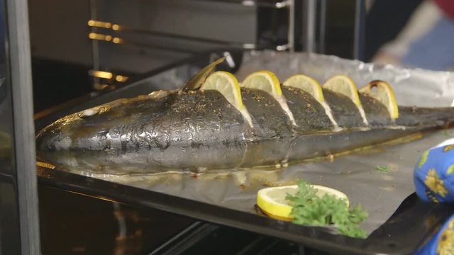 Cooking whole roasted fish seriola with lemon baked in the oven. Chef takes out baking sheet with cooked amberjack from the oven. Food preparation with electric cooker.