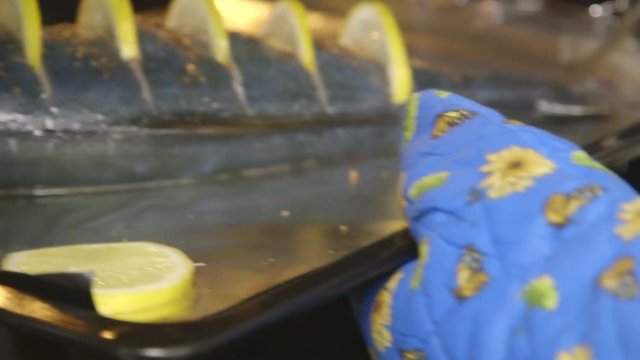 Cooking whole roasted fish seriola with lemon baked in the oven. Chef puts a baking sheet with raw amberjack takes out cooked fish from the oven. Edited sequence.