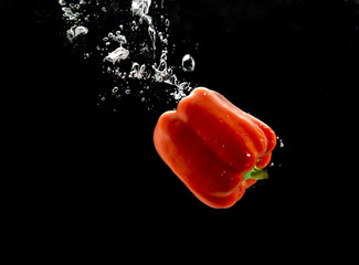 Red bell pepper falling into water with a trail of bubbles