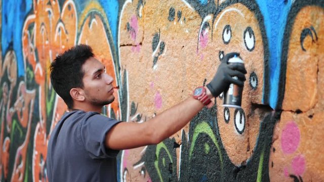 Handsome Talented Young Boy making a colorful graffiti with aerosol spray on urban street wall. Cinematic toned slow motion footage. Creative art. Side view