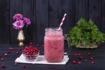 Cranberry juice smoothie shake in glass mug and raw cranberry on black wooden background, close up
