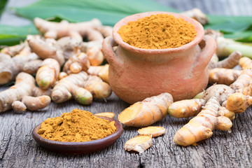 Turmeric powder in clay pot , turmeric capsules and fresh turmeric root on wooden background