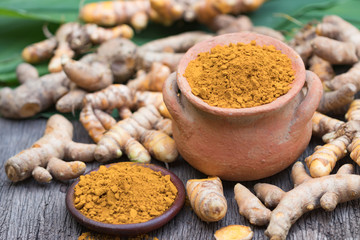Turmeric powder in clay pot , turmeric capsules and fresh turmeric root on wooden background