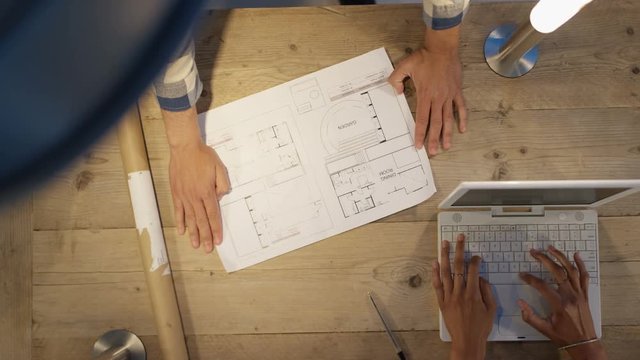 Unrecognizable team of architects in a meeting looking at floor plan. Overhead view looking down at workspace.