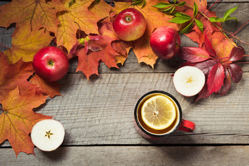 Warming cup of tea, decor of autumn leaves, apples on wooden board. Fall still life. Top view.