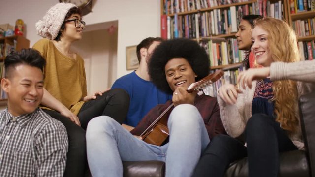 Happy young friends in shared apartment playing guitar and socializing.